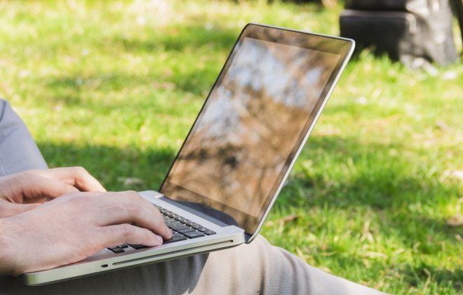 Persona sentada al aire libre, en el césped, con un ordenador portátil sobre la rodilla